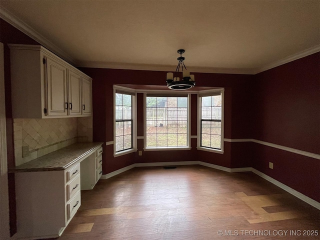 unfurnished dining area featuring a notable chandelier, light wood-style flooring, crown molding, and baseboards