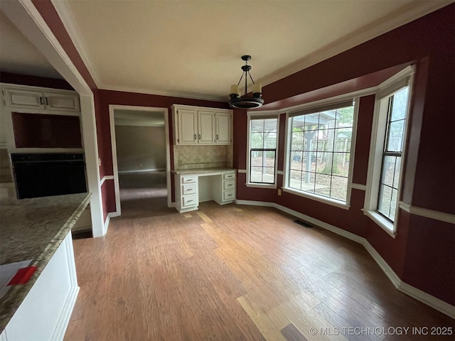 kitchen with visible vents, built in study area, ornamental molding, light wood-style floors, and backsplash