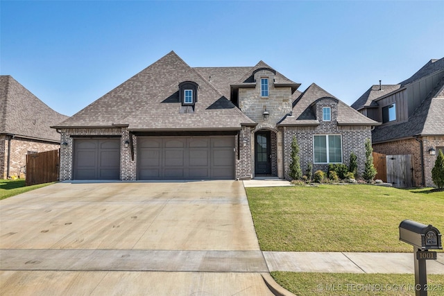 french provincial home with a front yard, concrete driveway, fence, and brick siding