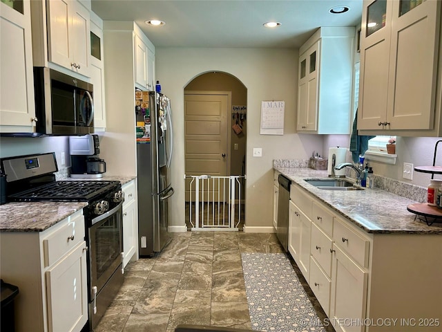 kitchen with a sink, arched walkways, appliances with stainless steel finishes, baseboards, and light stone countertops