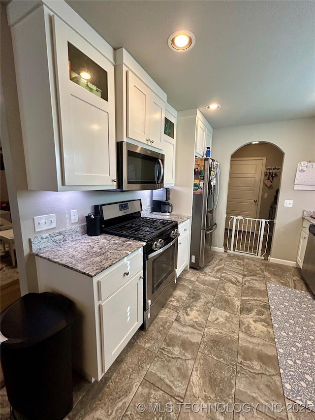 kitchen with arched walkways, white cabinets, appliances with stainless steel finishes, and light stone countertops