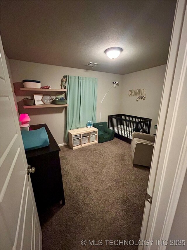 bedroom with a nursery area, visible vents, carpet floors, and a textured ceiling