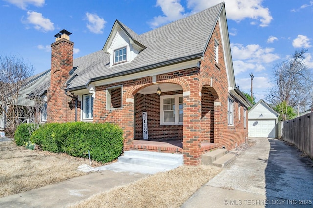 view of front of home featuring brick siding, covered porch, concrete driveway, and an outbuilding