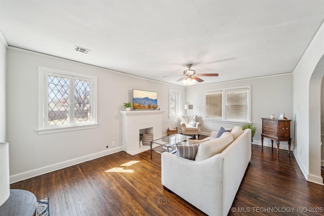 living area with visible vents, dark wood finished floors, arched walkways, a brick fireplace, and a wealth of natural light