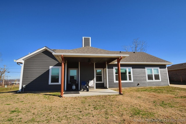 back of house featuring a lawn, a ceiling fan, a patio, a shingled roof, and a chimney