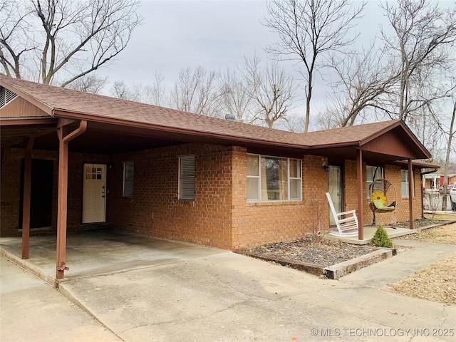 ranch-style house with brick siding, an attached carport, driveway, and roof with shingles