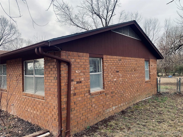 view of side of home with a gate, brick siding, and fence