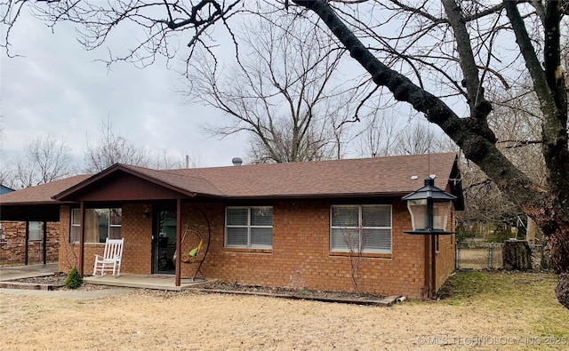 ranch-style home featuring a gate, fence, covered porch, a shingled roof, and brick siding