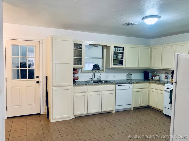 kitchen featuring white appliances, light tile patterned floors, visible vents, dark stone counters, and a sink