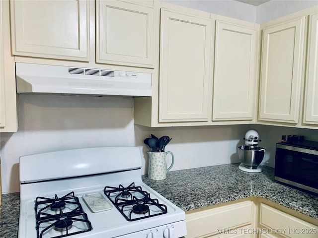 kitchen featuring dark countertops, stainless steel microwave, under cabinet range hood, white range with gas cooktop, and white cabinetry