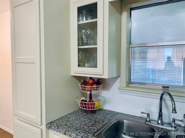 details with dark stone countertops, white cabinetry, glass insert cabinets, and a sink