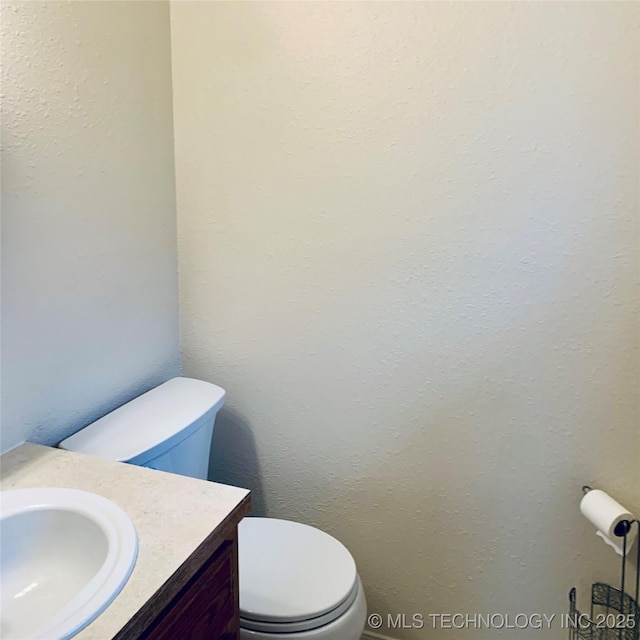 bathroom featuring vanity, toilet, and a textured wall