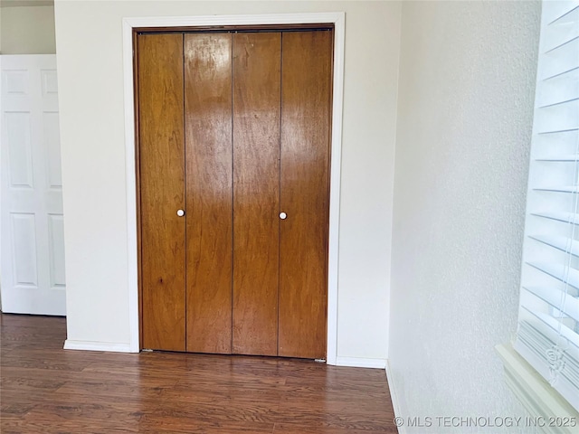 unfurnished bedroom with a closet, baseboards, and dark wood-type flooring