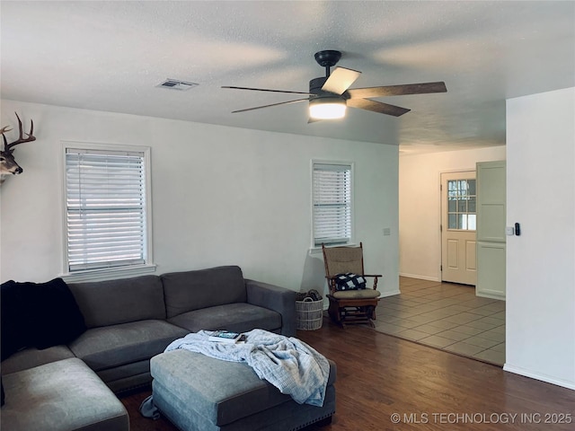 living area with visible vents, a ceiling fan, a textured ceiling, wood finished floors, and baseboards