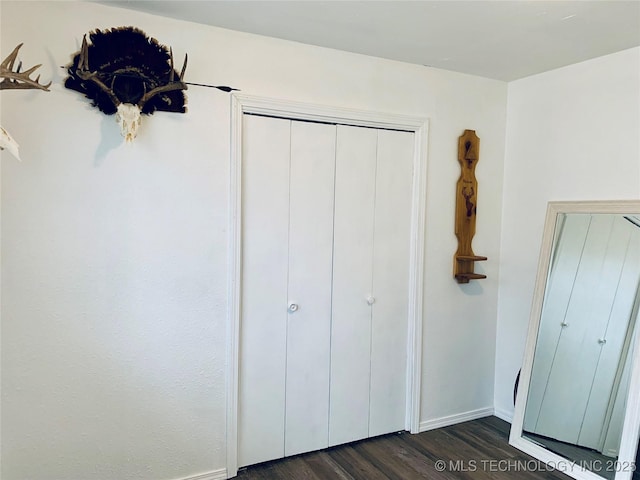 unfurnished bedroom featuring a closet, baseboards, and dark wood-type flooring