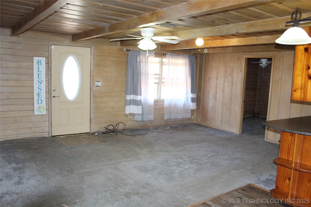 carpeted entrance foyer with wooden ceiling, wooden walls, a ceiling fan, and beamed ceiling