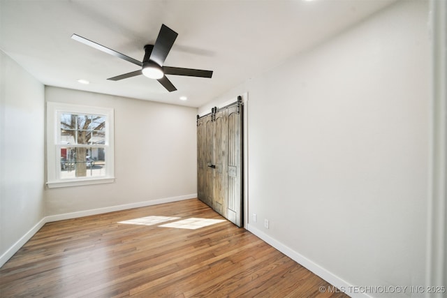 interior space with a ceiling fan, wood finished floors, baseboards, recessed lighting, and a barn door