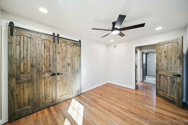 unfurnished bedroom with recessed lighting, a barn door, baseboards, and wood finished floors