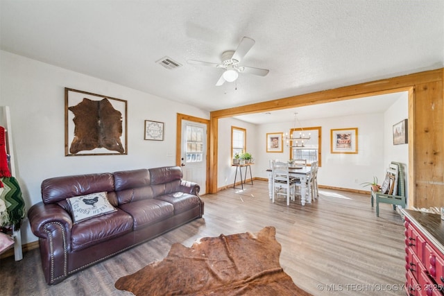 living room featuring light wood finished floors, visible vents, baseboards, a textured ceiling, and a ceiling fan