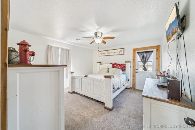 bedroom featuring visible vents, light colored carpet, a textured ceiling, and ceiling fan