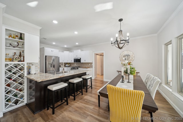 kitchen featuring appliances with stainless steel finishes, white cabinets, a peninsula, crown molding, and an inviting chandelier