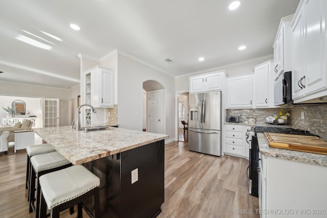 kitchen featuring light wood-type flooring, a sink, arched walkways, appliances with stainless steel finishes, and white cabinets