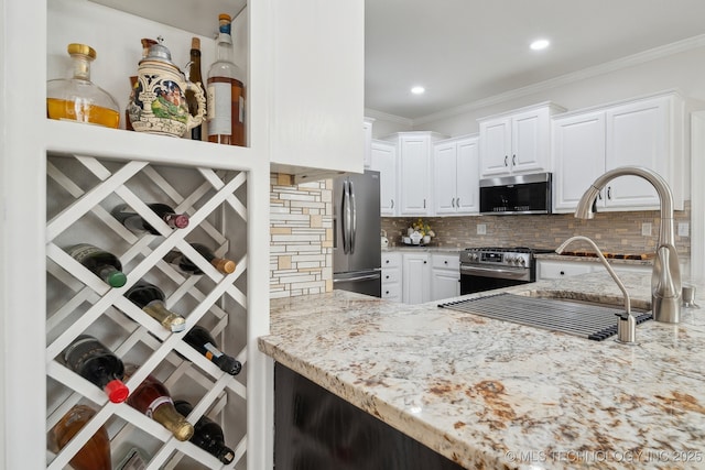 kitchen with light stone counters, decorative backsplash, white cabinets, appliances with stainless steel finishes, and crown molding