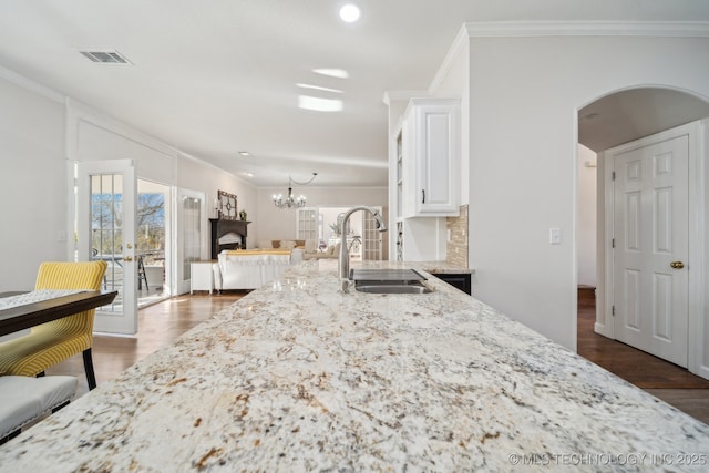 kitchen with visible vents, ornamental molding, light stone counters, arched walkways, and a sink