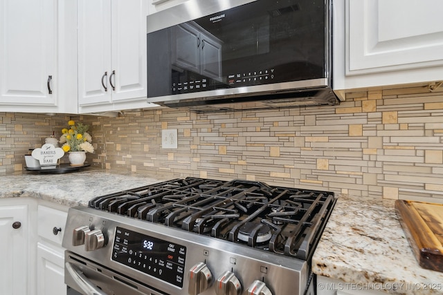 room details with backsplash, white cabinets, stainless steel appliances, and light stone countertops