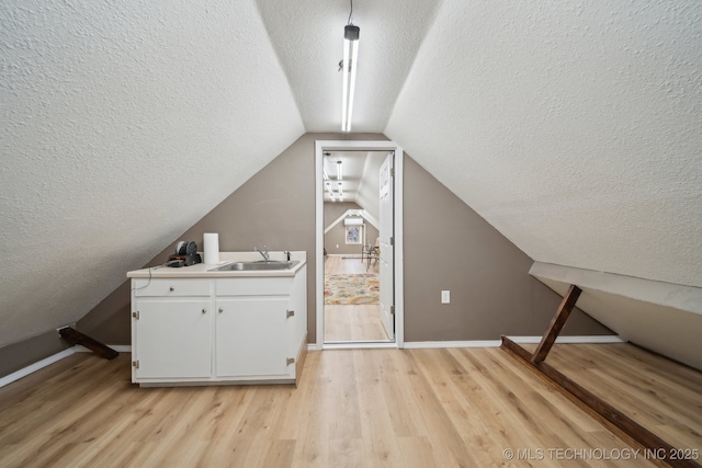 bonus room with a sink, baseboards, light wood-style floors, and vaulted ceiling