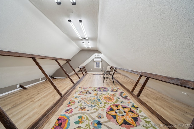 interior space with a textured ceiling, light wood-type flooring, and vaulted ceiling