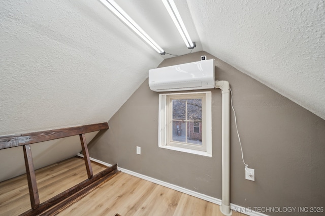 additional living space featuring baseboards, lofted ceiling, a wall unit AC, wood finished floors, and a textured ceiling