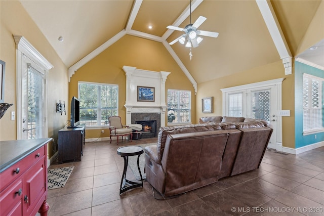 living room featuring baseboards, ceiling fan, a lit fireplace, high vaulted ceiling, and dark tile patterned flooring