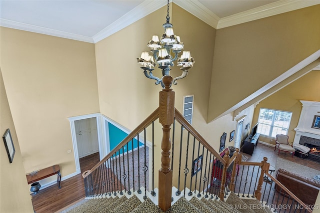 stairs featuring crown molding, a high ceiling, a notable chandelier, and a lit fireplace