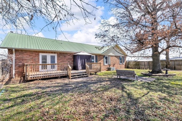 back of house featuring fence, brick siding, french doors, and metal roof