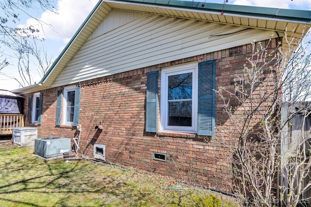 view of side of property featuring brick siding, a yard, and central AC