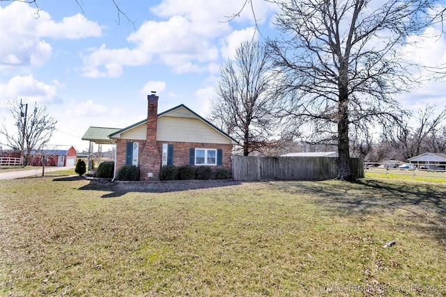 view of side of home featuring brick siding, a chimney, a lawn, and fence