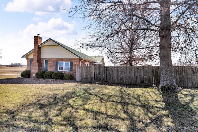 view of side of property with brick siding, a lawn, a chimney, and fence