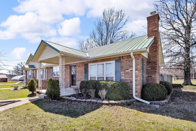 view of front of home with a standing seam roof, a front yard, metal roof, brick siding, and a chimney