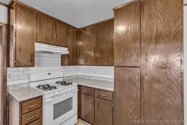 kitchen with tasteful backsplash, under cabinet range hood, white gas stove, light countertops, and a textured ceiling