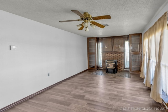 unfurnished living room featuring a wood stove, light wood-style floors, baseboards, and a textured ceiling