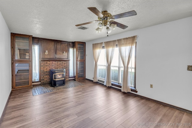 unfurnished living room with a wood stove, wood finished floors, visible vents, and a textured ceiling