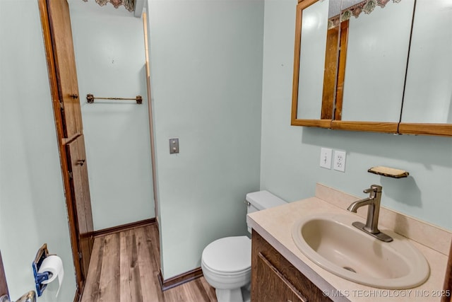 half bathroom featuring vanity, toilet, wood finished floors, and baseboards