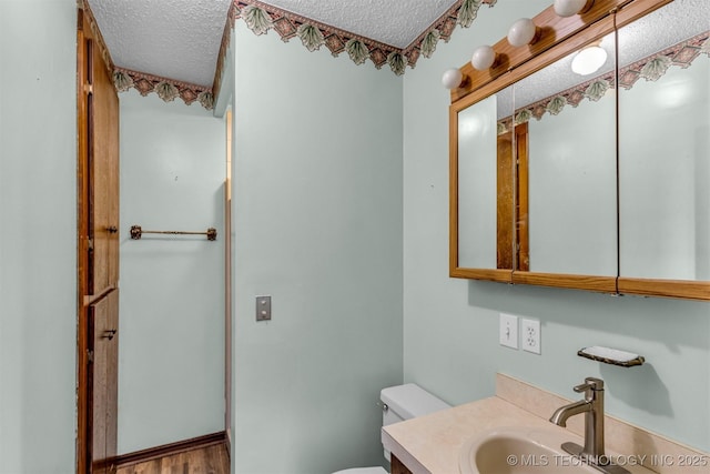 bathroom featuring a textured ceiling, wood finished floors, vanity, and toilet