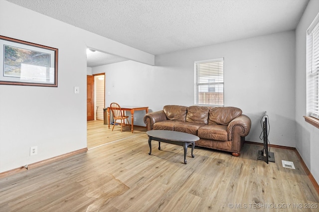 living area with visible vents, light wood-style flooring, a textured ceiling, and baseboards