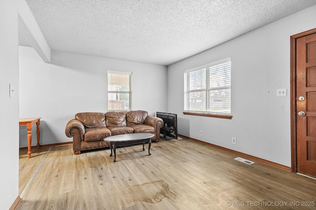 living room featuring visible vents, a textured ceiling, baseboards, and wood finished floors