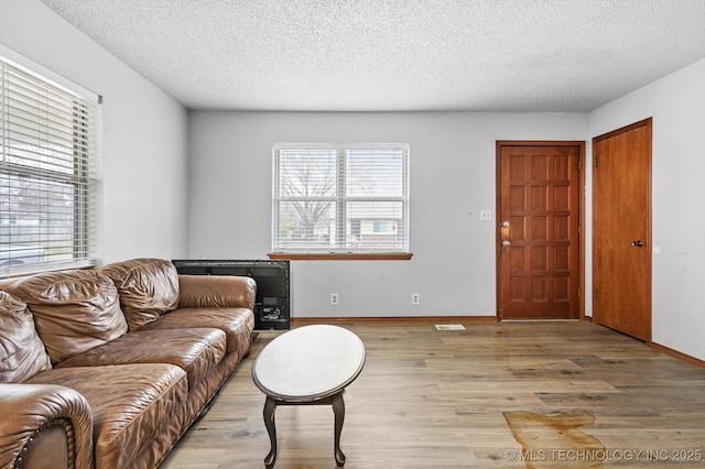 living room featuring visible vents, light wood-style floors, baseboards, and a textured ceiling