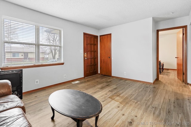 living area featuring visible vents, a textured ceiling, light wood-type flooring, and baseboards