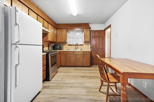 kitchen featuring freestanding refrigerator, a sink, light countertops, electric stove, and light wood-style floors