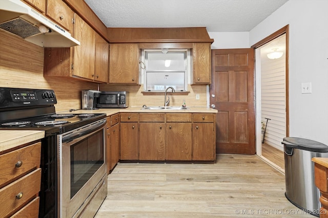 kitchen with under cabinet range hood, stainless steel appliances, brown cabinetry, and a sink